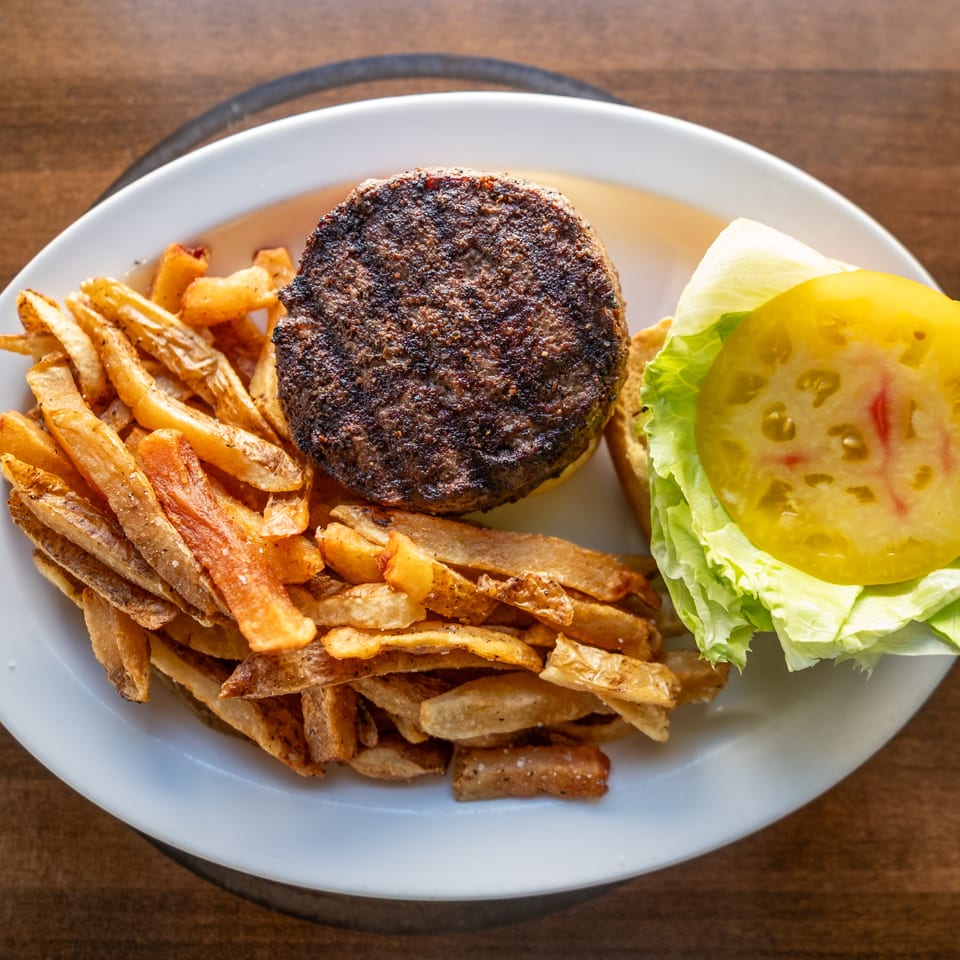 Grilled burger with lettuce and tomato beside a generous serving of golden fries on a white plate.