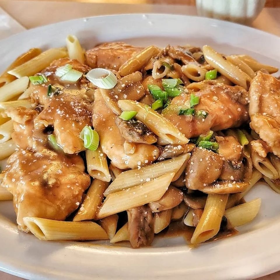 Penne pasta with chicken, mushrooms, and sauce, garnished with green onions and cheese.